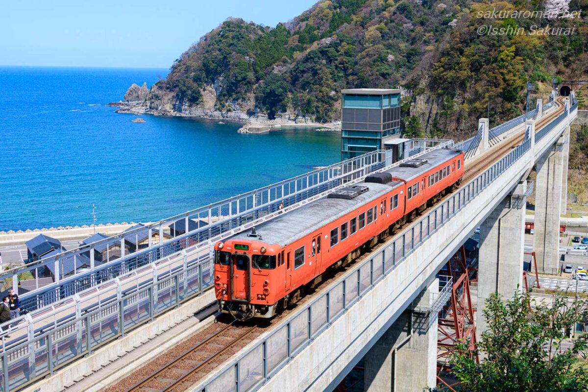 日本海を背景に新しいコンクリート製の余部橋梁を渡る赤い列車