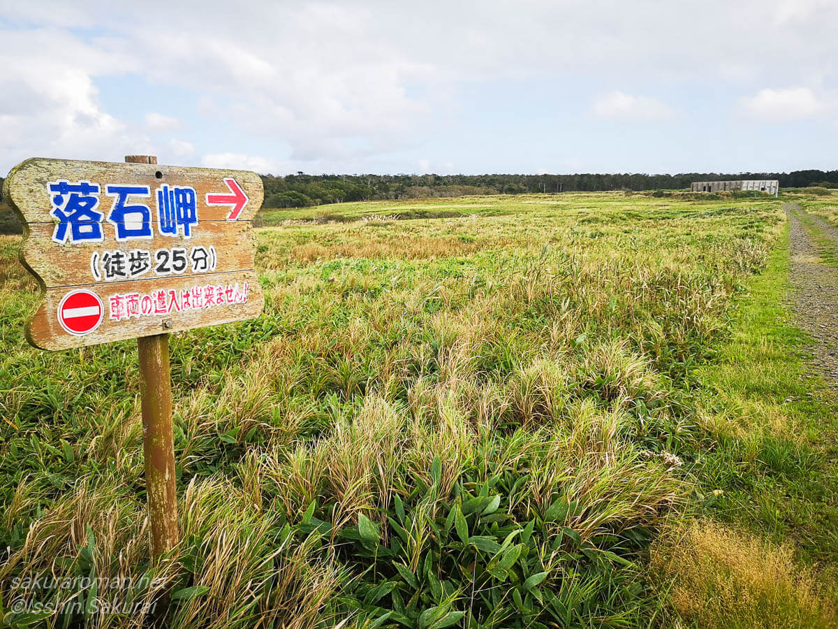落石岬へ徒歩25分と示す木製案内板と草原のフットパス入口